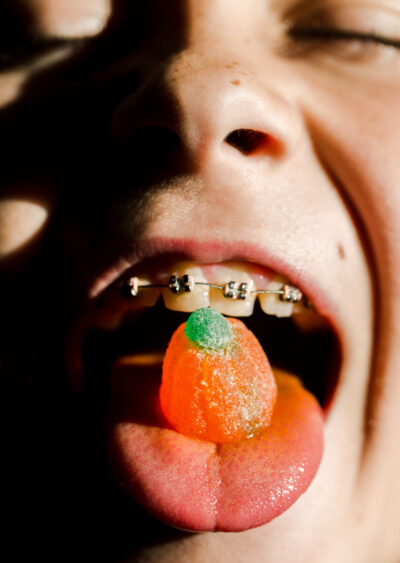 Close up shot of a young child, with braces, sticking their tongue out with a halloween sweet on the tip of their tongue.